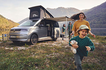 Familie beim Campingurlaub mit Volkswagen Camper an einem See