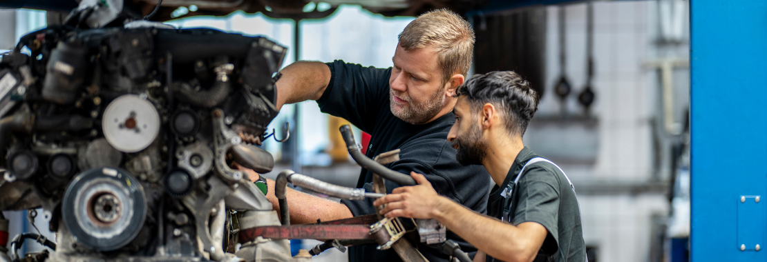 Zwei Kfz-Mechatroniker arbeiten am Motor eines Fahrzeugs